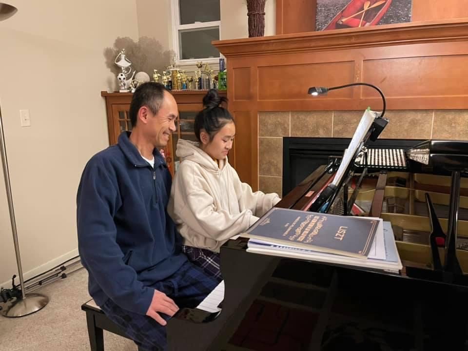 A parent and student playing the piano together at home