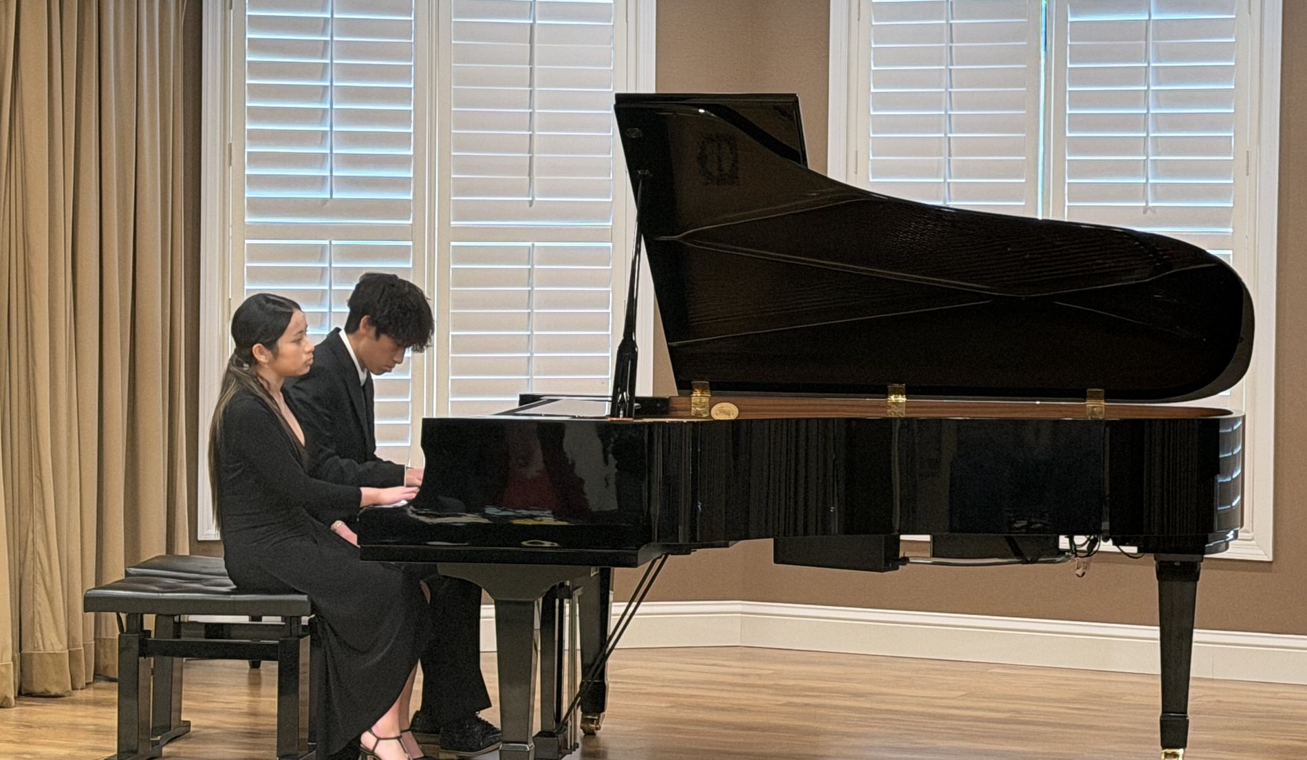 Two Caruth Piano Studio students performing a duet on a concert grand at a recital hall