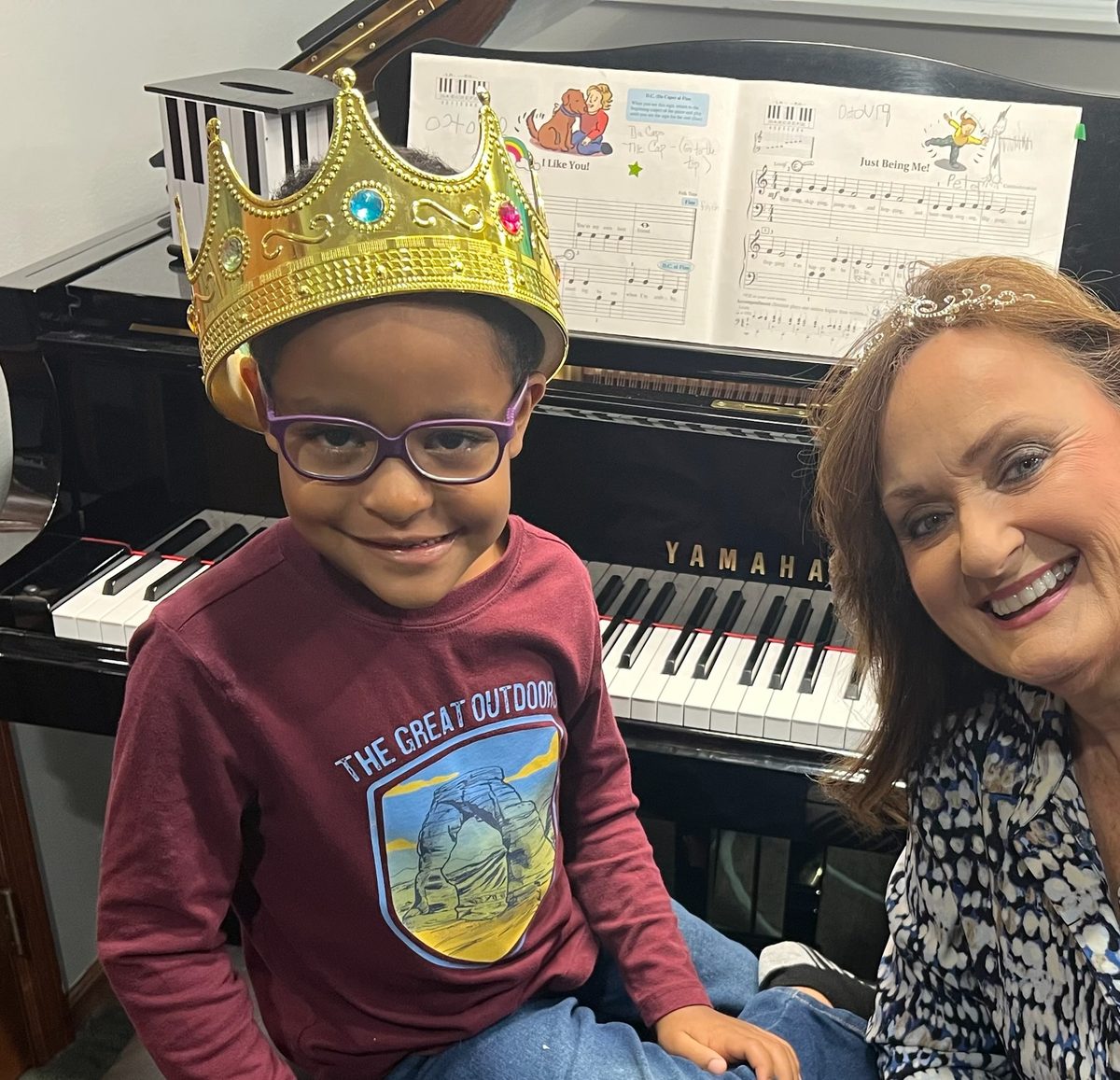 Cyndie Caruth at the piano with a young beginner wearing a paper crown